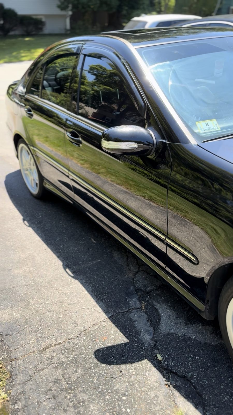 Side profile of a black Mercedes C-Class with mirror-gloss paint reflecting a green lawn